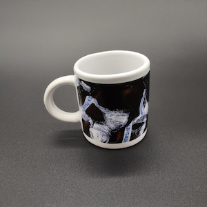 May include: A white ceramic coffee mug with a black and white Hershey's Kisses design. The mug has a white interior and a small, curved handle. The Hershey's Kisses logo is visible on the mug.