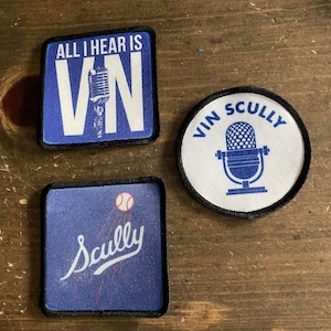 May include: Three blue and white embroidered patches with black borders. One patch is square and says "All I hear is Vin" with a microphone image. Another patch is round and says "Vin Scully" with a microphone image. The third patch is square and says "Scully" with a baseball image.