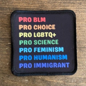 May include: A black square patch with white text in a rainbow color scheme. The text reads "PRO BLM", "PRO CHOICE", "PRO LGBTQ+", "PRO SCIENCE", "PRO FEMINISM", "PRO HUMANISM", and "PRO IMMIGRANT".