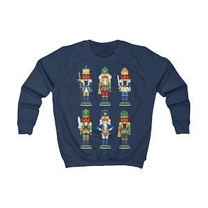 Puede incluir: Una sudadera azul marino con un diseño colorido de seis figuras de cascanueces. Los cascanueces llevan todos sombreros y uniformes de diferentes colores.