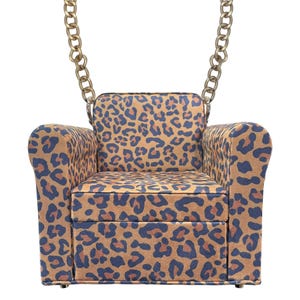 May include: A miniature armchair-shaped handbag with a leopard print pattern in brown and navy blue. The bag has a gold-colored chain strap. The design mimics a small sofa, complete with armrests and a seat.