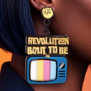 May include: Gold and black acrylic earrings with a television screen design. The screen has a rainbow pattern and the text "Revolution Bout To Be" is written in gold letters.