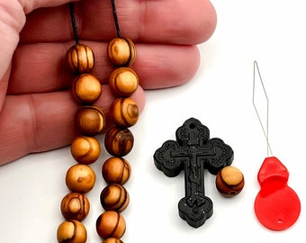 Puede incluir: Un collar de cuentas de oración de madera con un colgante de cruz negra. El collar está hecho de cuentas de madera marrón con un patrón rayado. El colgante de cruz tiene un acabado negro y está decorado con detalles intrincados. El collar está encordado en un cordón negro.
