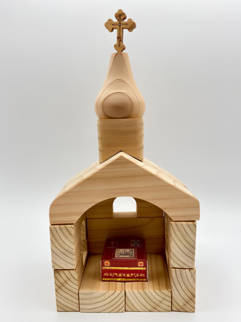 Pode incluir: Modelo de igreja em madeira com uma cruz no topo. A igreja &eacute; constru&iacute;da com blocos de madeira de cor clara, com um livro vermelho no interior. O design lembra uma igreja tradicional.