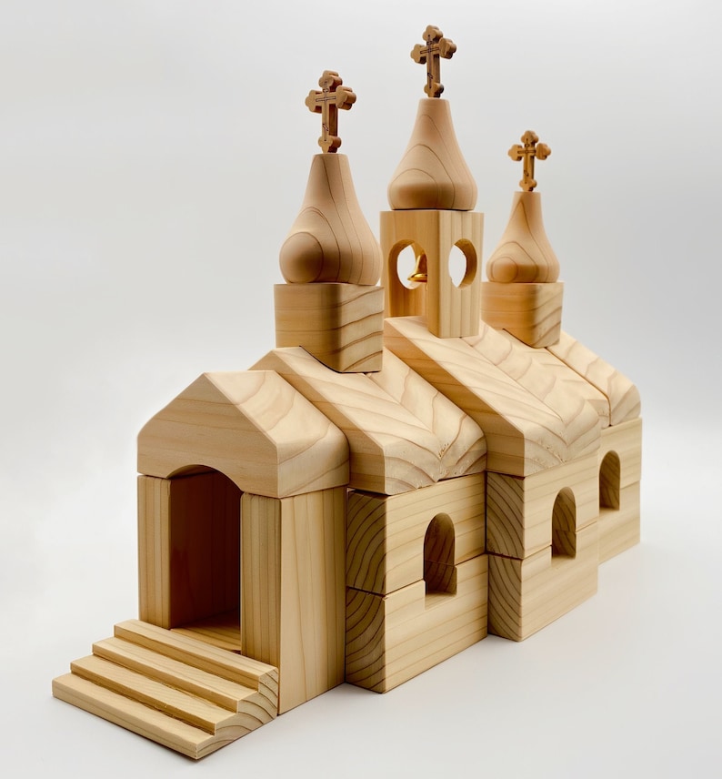 Pode incluir: Um modelo de igreja de madeira com tr&ecirc;s torres sineiras encimadas por cruzes. O edif&iacute;cio tem janelas arqueadas e uma pequena torre sineira. O modelo &eacute; feito de madeira clara e apresenta um design detalhado, incluindo degraus que conduzem &agrave; entrada.