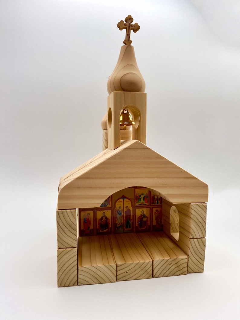 Pode incluir: Modelo de igreja em madeira com uma cruz no topo. O modelo apresenta uma torre sineira e um interior com &iacute;cones religiosos. A estrutura &eacute; feita de madeira clara e tem um design simples em blocos.