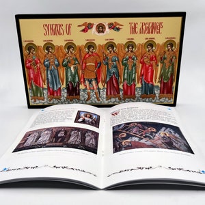 May include: A closed book with a colorful image of angels on the front cover. The book is open to a page with text and images about angels. The text on the front cover reads "Symbols of the Angels".