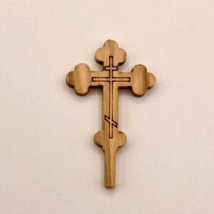 Op de afbeelding: Een houten kruis met een traditioneel orthodox ontwerp. Het kruis is gesneden uit lichtbruin hout en heeft een eenvoudig, elegant ontwerp.