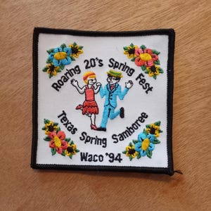 May include: A white embroidered patch with a black border. It features a cartoon couple dancing, surrounded by flowers. The text reads "Roaring 20's Spring Fest Texas Spring Jamboree Waco '94".