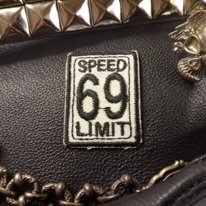May include: A white and black embroidered patch with the text "SPEED LIMIT 69" on a black leather background.