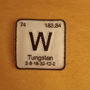 May include: A white square patch with black stitching around the edges. The patch has the chemical symbol "W" for Tungsten, the atomic number "74", the atomic weight "183.84", and the electron configuration "2-8-18-32-12-2".