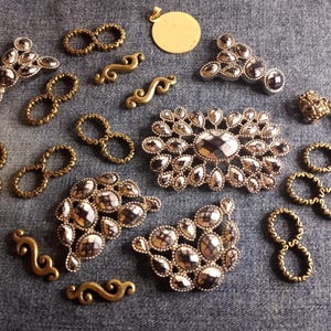 May include: Assortment of gold-toned metal jewelry findings and embellishments, including decorative loops, swirls, and ornate pieces with rhinestones.