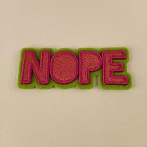May include: A green felt patch with the word "NOPE" embroidered in pink.