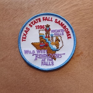 May include: A white embroidered patch with a blue border. The patch features a map of Texas with the text "Texas State Fall Jamboree 1996 Wichita Falls" and "Wild West Rendezvous at the Falls".