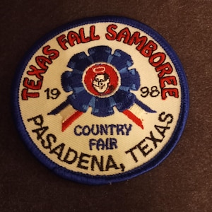 May include: A white and blue embroidered patch with the text "Texas Fall Samboree 1998 Pasadena, Texas Country Fair". The patch features a cartoon character with a halo and a blue ribbon.