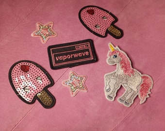 May include: A set of iron-on patches featuring a unicorn, two pink popsicles, two sparkly stars, and a black and pink patch with the text "vaporwave".
