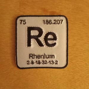 May include: A white and black embroidered patch with the chemical element symbol for Rhenium, Re, with the atomic number 75 and atomic weight 186.207. The patch also includes the element's name, Rhenium, and its electron configuration, 2-8-18-32-13-2.