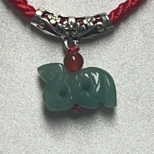 May include: A red string necklace with a jade green animal pendant and a silver floral design. The pendant is attached to the string with a silver bead.