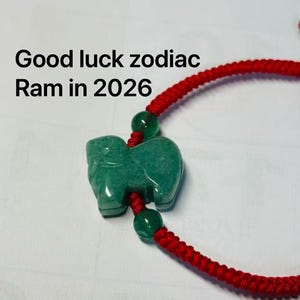 Puede incluir: Un colgante de jade verde con forma de carnero, con un cordón rojo. El texto "Good luck zodiac Ram in 2026" aparece encima. Un amuleto de la suerte.