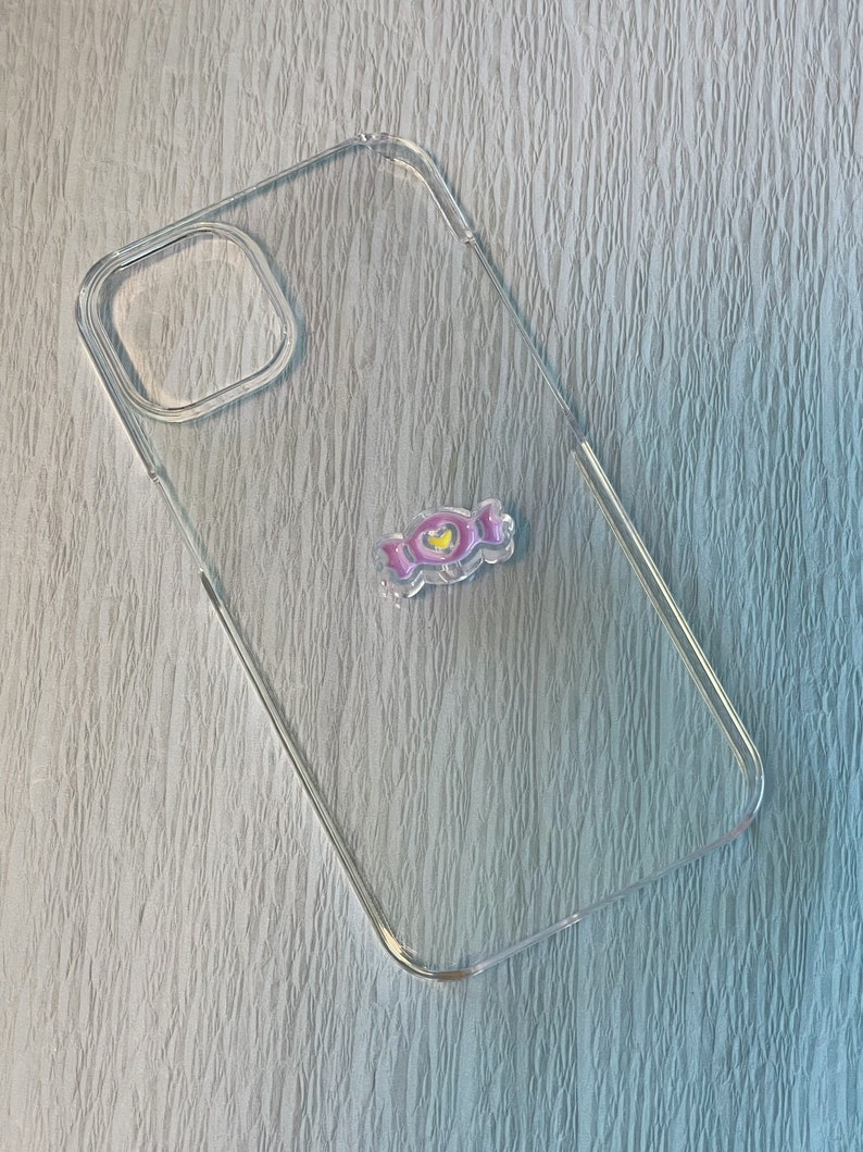 Op de afbeelding: Een transparante telefoonhoes met een roze en gele telefoonhouder in de vorm van een snoepje.