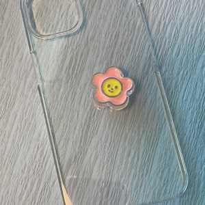 Op de afbeelding: Een transparante telefoonhoes met een roze bloemsticker met een gele smiley in het midden.