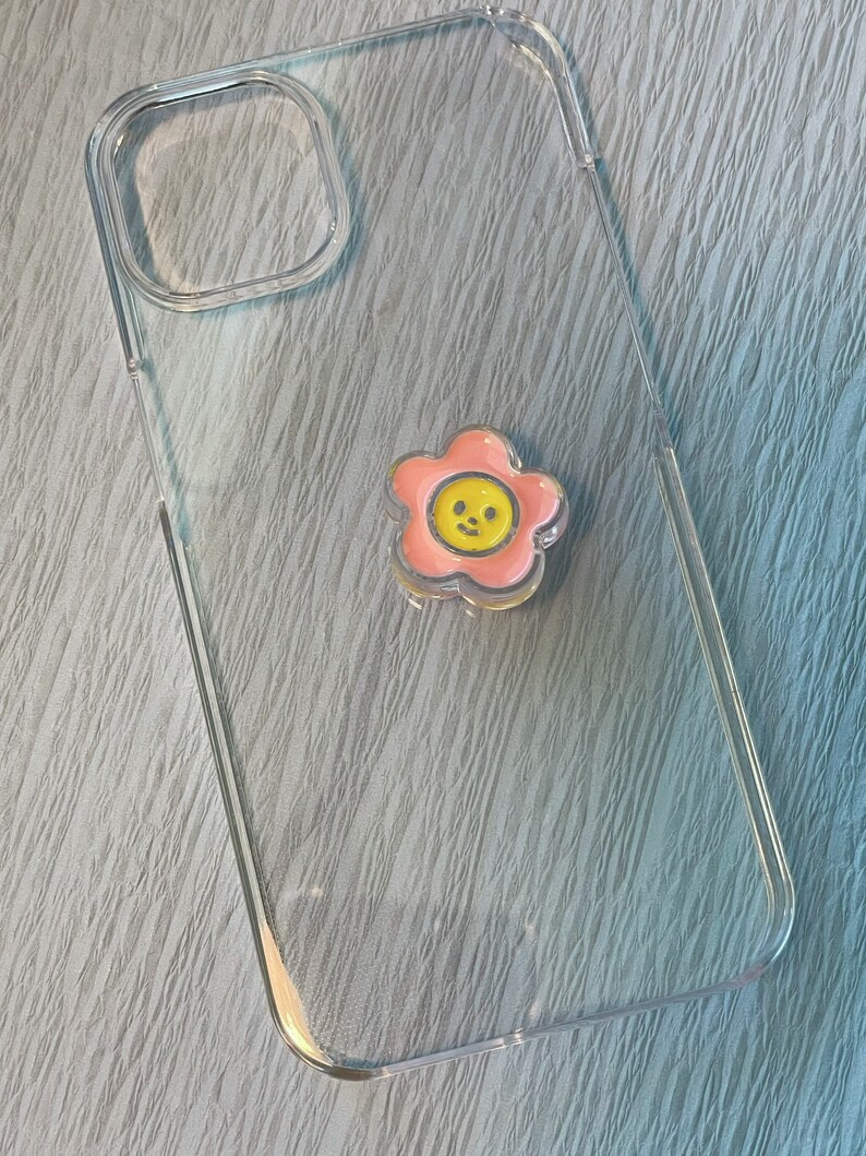 Op de afbeelding: Een transparante telefoonhoes met een roze bloemsticker met een gele smiley in het midden.