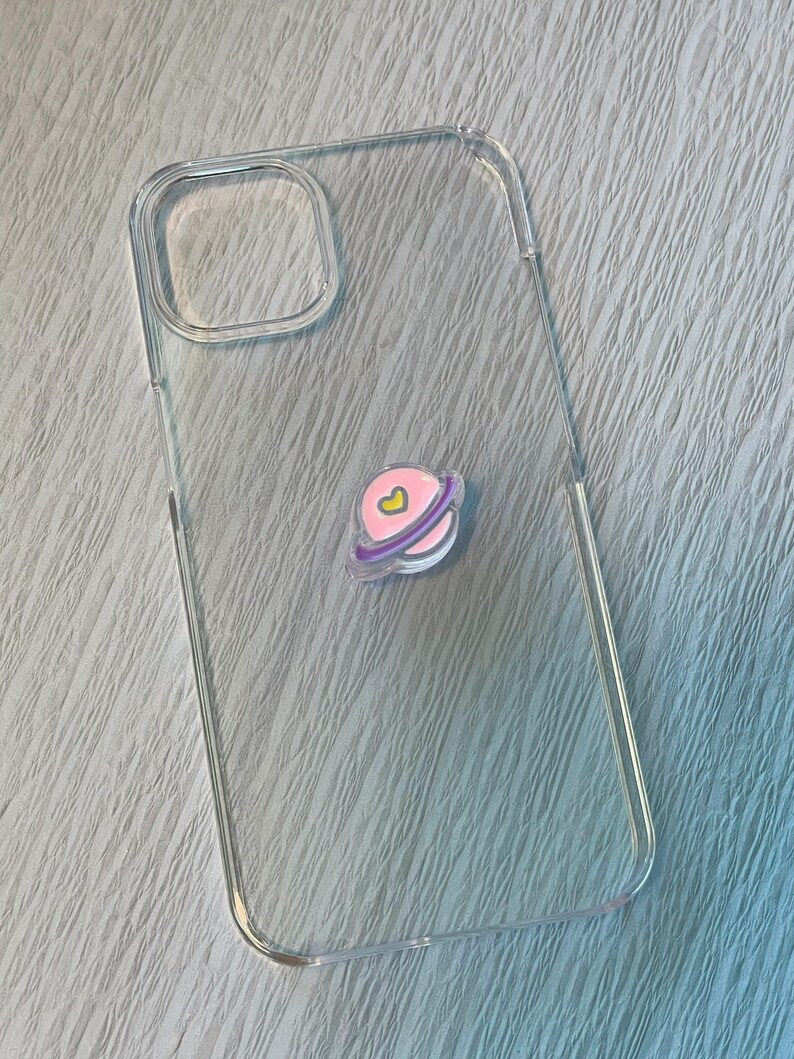 Op de afbeelding: Een transparante telefoonhoes met een roze en paarse planeet sticker met een geel hartje.