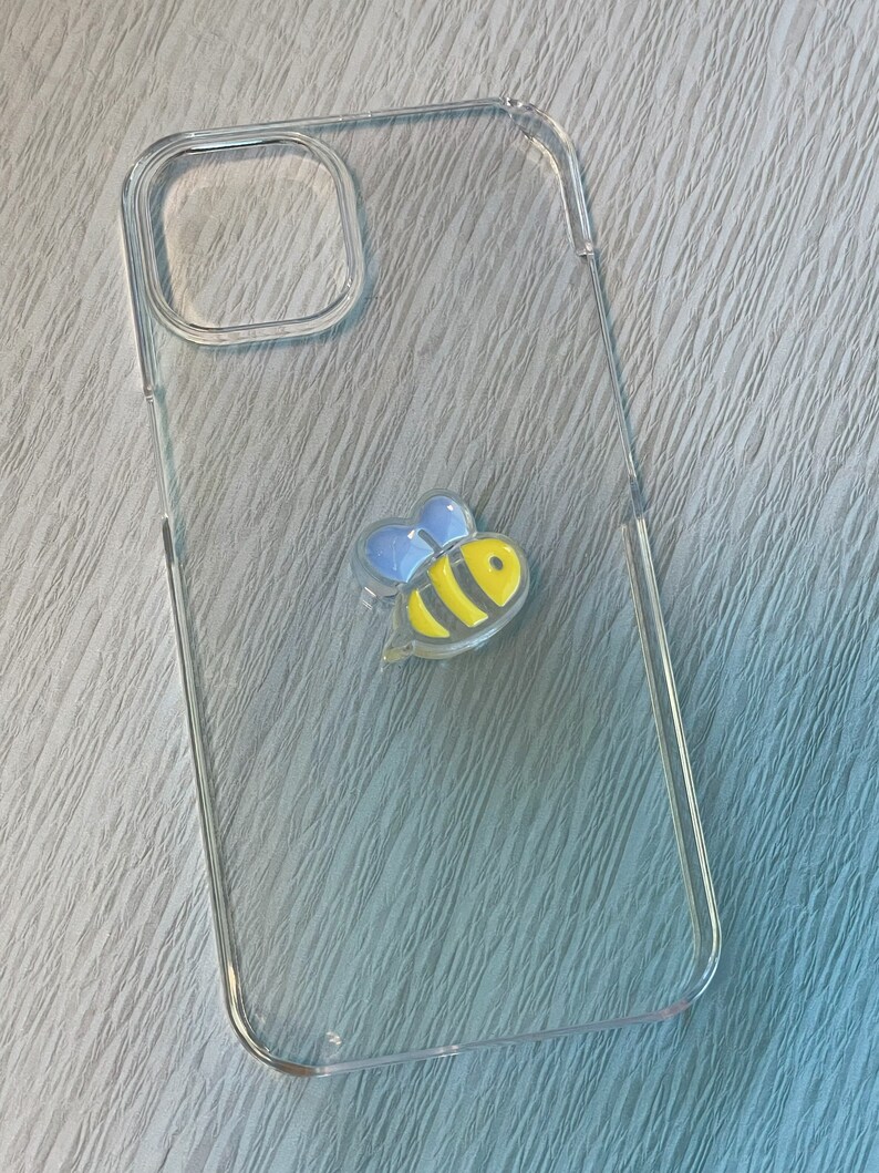 Op de afbeelding: Een transparante telefoonhoes met een geel en zwart bijenontwerp. De bij heeft blauwe vleugels.