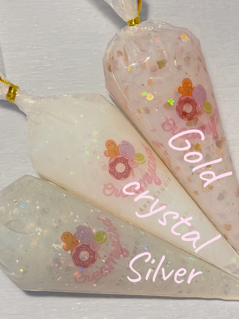 May include: Three clear plastic bags filled with glitter and decorative elements. The bags are labeled "Gold", "Crystal", and "Silver". Each bag features a sticker with a gingerbread man, donut, and candy design.
