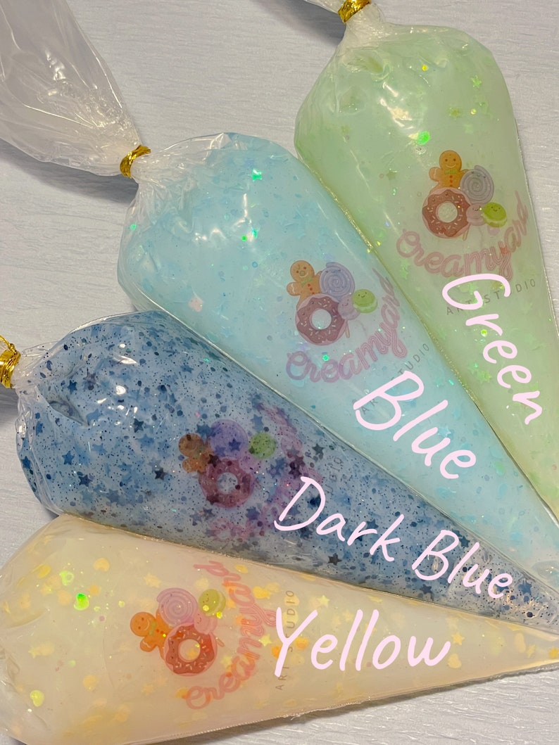 May include: Four clear plastic bags filled with colorful, glittery slime. The bags are labeled with the colors: Yellow, Dark Blue, Blue, and Green. Each bag is sealed with a gold twist tie and features a logo with a donut and gingerbread man.