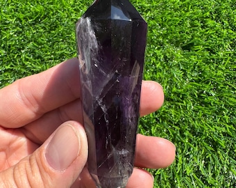 May include: A dark purple amethyst crystal point with a double-terminated shape. The crystal is smooth and polished, with a pointed tip and a flat base.