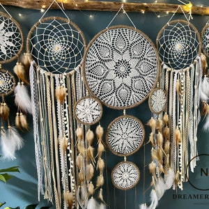May include: A set of seven white and brown dreamcatchers with intricate crocheted designs and feathers hanging from the bottom. The dreamcatchers are arranged in a row against a blue wall.