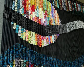 May include: A colorful wall hanging made of woven black and multi-colored cords. The cords are woven in a pattern that creates a wave-like design. The cords are woven in a variety of colors, including red, blue, green, yellow, and white.