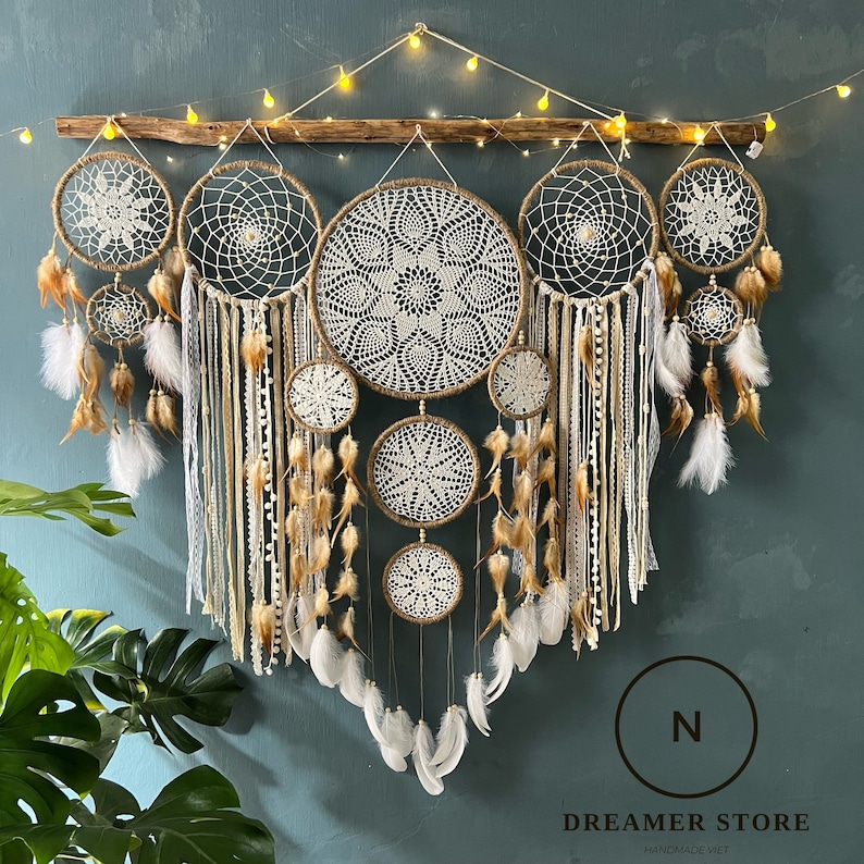 May include: A large dreamcatcher wall hanging with multiple layers of white crocheted circles and brown feathers. The dreamcatcher is decorated with white and brown ribbons and beads.