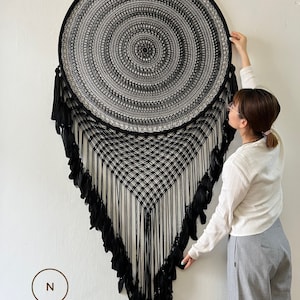 May include: A large black dreamcatcher with a circular woven design and feather accents. The dreamcatcher is hanging on a white wall. The text "DREAMER STORE HANDMADE GIFT" is visible at the bottom of the image.