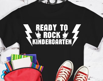 May include: Black t-shirt with white text that reads "Ready to Rock Kindergarten" with a lightning bolt and rock and roll hand gesture on either side of the text.