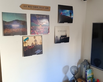 May include: A white wall with a wooden sign that reads "LA REUNION 9342 KM A pie nou gain pa!" and several vinyl records displayed on the wall. The records are titled "Supertramp", "The Postal Service", and "Ravinsky".