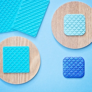 May include: Four wooden coasters with blue and teal patterned tiles. The tiles have a mermaid scale design.