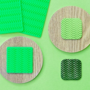 May include: Four green squares with a wavy pattern, two are on a wooden circle, one is on a larger wooden circle, and one is on a green background.