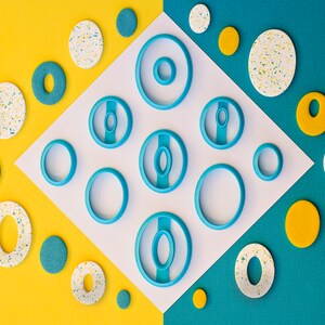 May include: A set of blue plastic cookie cutters in various sizes and shapes, arranged on a white background with yellow and blue accents.