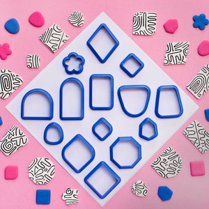 May include: A set of 15 blue plastic cookie cutters in various shapes, including circles, squares, rectangles, and geometric designs, on a pink background.