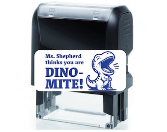 May include: A black and white self-inking stamp with a blue dinosaur graphic and the text "Ms. Shepherd thinks you are DINO-MITE!"