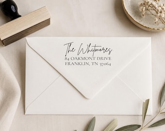 May include: A white envelope featuring a black ink stamp with the text The Whitmores, 84 OAKMONT DRIVE, FRANKLIN, TN 37064. The stamp uses a combination of a handwritten script font for the name and a clean serif font for the address details.