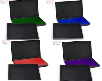 May include: Six black ink pads with different colored ink pads. The ink pads are open and show the ink colors: green, blue, red, purple, black, and brown.