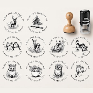 May include: A collection of twelve circular black ink stamps featuring nature-themed illustrations including a deer, pine tree, birds, bear, ducks, fox, and owls. Each stamp includes the text FROM THE LIBRARY OF HARRY MCDONALD. A wooden handle stamp and a black self-inking stamp are shown.