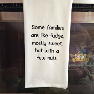 May include: White kitchen towel with black text that reads "Some families are like fudge, mostly sweet, but with a few nuts". The towel is hanging on a stainless steel oven.