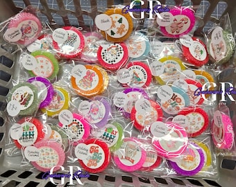 May include: A basket filled with various round, colorful, and scented air fresheners. Each air freshener is individually packaged and labeled with names like "Pistachio Caramel," "Holiday Festival," and "Cactus Blossom." The labels feature festive graphics.