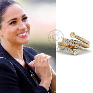 May include: A gold-colored ring with a spiral design, adorned with multiple small diamonds and three larger, bezel-set diamonds. The ring is shown on a white background.