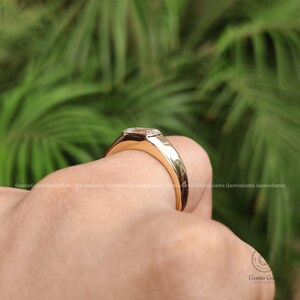 May include: A gold ring featuring a rectangular emerald-cut gemstone set in a smooth, polished metal band. The ring has a low-profile bezel setting that holds the clear stone securely, showcasing a clean, reflective surface and a solid gold band.