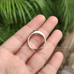 May include: A rose gold ring featuring a smooth, polished band and a rectangular setting at the top. The metal has a warm, pinkish hue and a reflective surface. The ring is shown from a top-down perspective, highlighting the circular band shape.